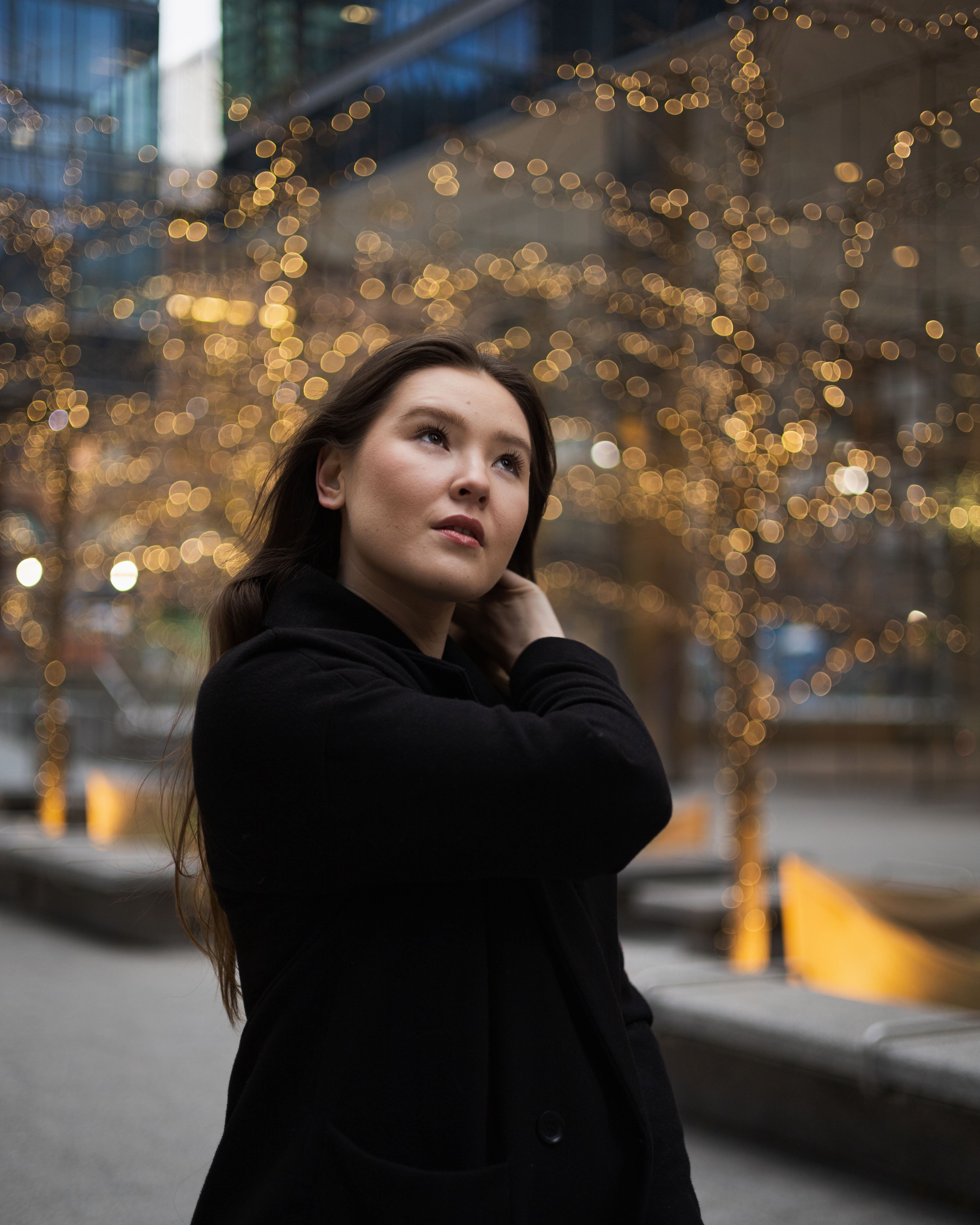 A woman stroking her hair in front of trees with fairy lights