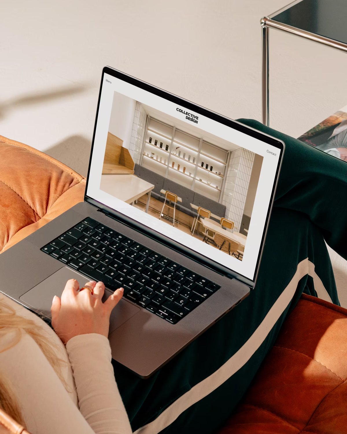 Person lounging in an armchair with a laptop on their lap, displaying the Collective Design website featuring an interior design project portfolio.