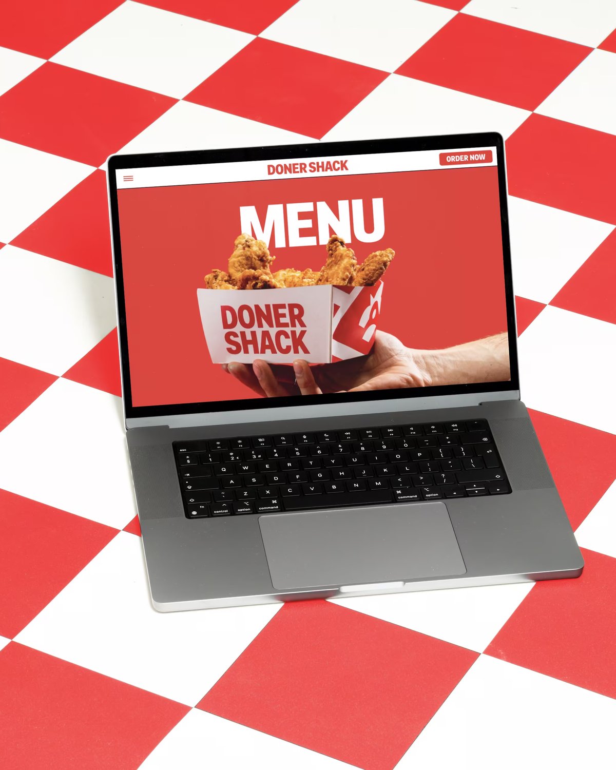 A open laptop resting on a red-and-white checkered surface displaying the Doner Shack menu page.