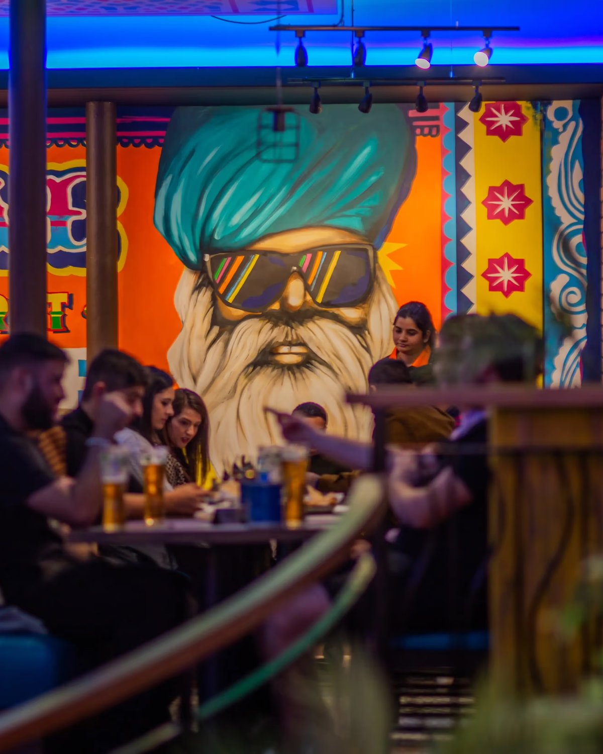 Vibrant Indian restaurant dining area featuring a colorful wall mural of a man in a turquoise turban and sunglasses.