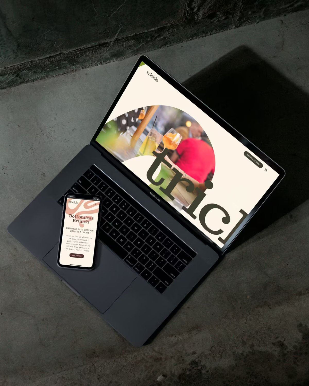 Website and mobile website mockups for Trickle displayed on a laptop screen and smartphone resting on a dark concrete surface.