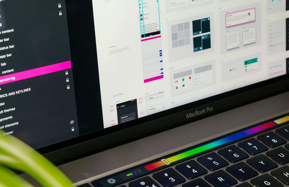 A MacBook screen displaying a design editor with UI component libraries, layout grids, and mobile wireframes.