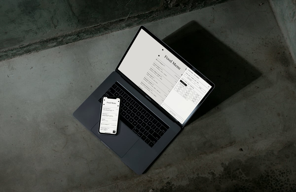 Laptop and smartphone displaying a responsive, filterable digital restaurant menu and dietary filter drawer set against a dark concrete background.